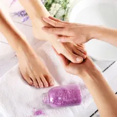 Relaksacyjny masaż stóp to klucz do tego, jak zrobić pedicure w domu. Fioletowa sól do kąpieli i biały ręcznik tworzą atmosferę domowego spa.