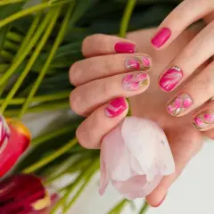 Dłonie z manicurem french zdobionym motywem tulipanów, otoczone bukietem różowych kwiatów.