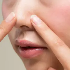 Dłonie dotykają nosa, ukazując drobne niedoskonałości i nadmiar sebum na twarzy.