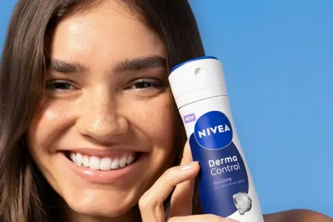 Uśmiechnięta kobieta trzyma NIVEA Derma Control, idealny produkt na swędzenie pod pachami.