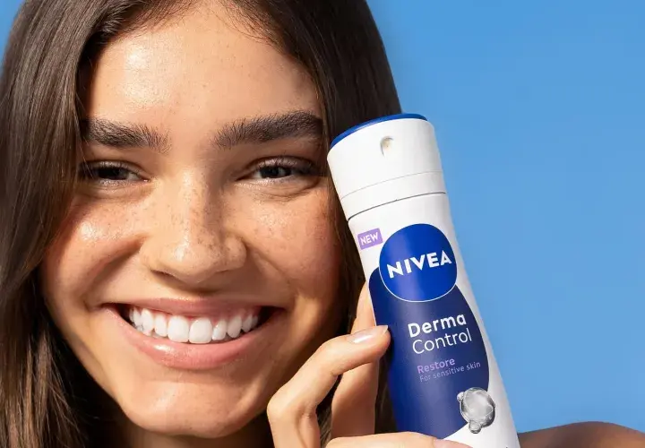 Uśmiechnięta kobieta trzyma NIVEA Derma Control, idealny produkt na swędzenie pod pachami.