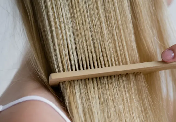 Delikatne rozczesywanie blond włosów drewnianym grzebieniem. Keratyna na co? Na zdrowe i lśniące włosy.