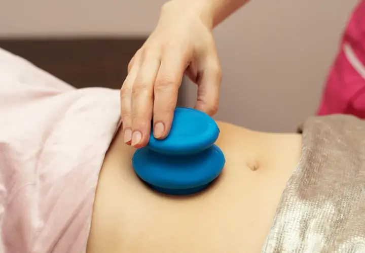 Dłoń terapeuty wykonuje masaż bańką chińską na brzuchu. Choć zabieg ma wiele zalet, warto znać jego potencjalne masaż bańką chińską efekty uboczne.