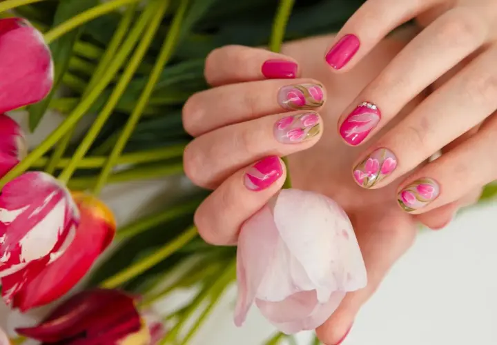 Dłonie z manicurem french zdobionym motywem tulipanów, otoczone bukietem różowych kwiatów.