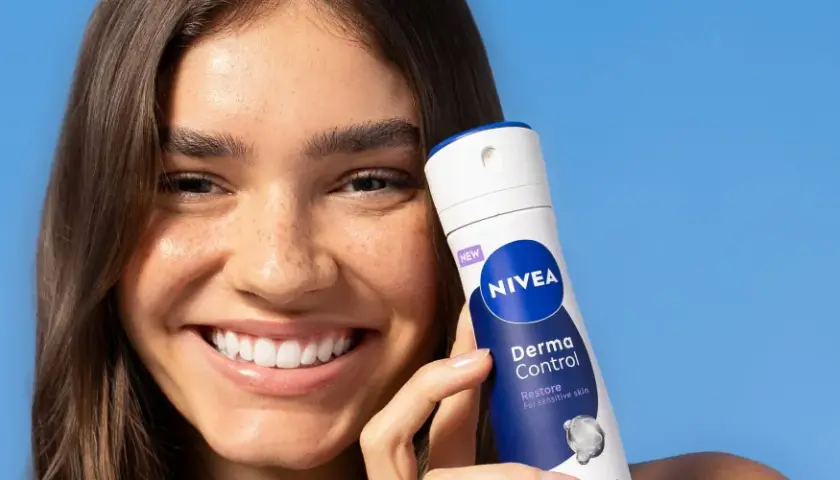 Uśmiechnięta kobieta trzyma NIVEA Derma Control, idealny produkt na swędzenie pod pachami.