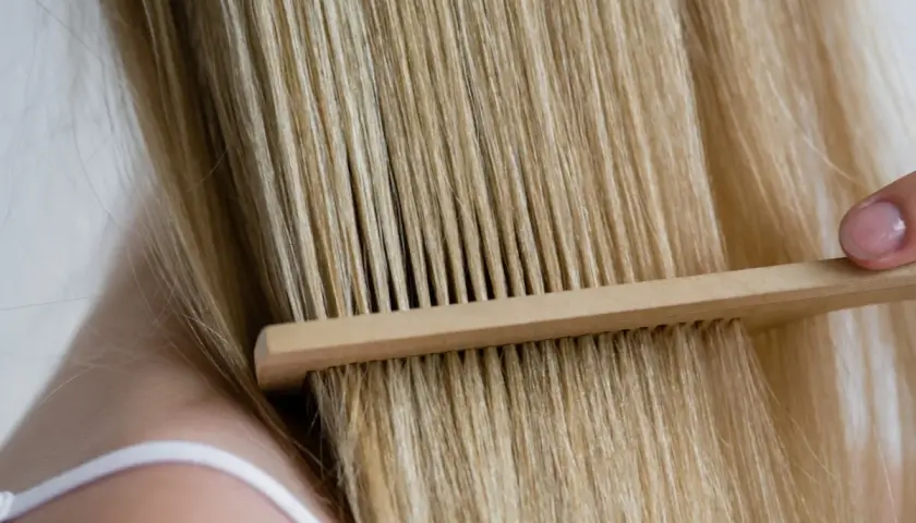 Delikatne rozczesywanie blond włosów drewnianym grzebieniem. Keratyna na co? Na zdrowe i lśniące włosy.