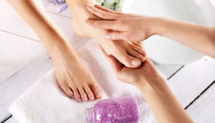 Relaksacyjny masaż stóp to klucz do tego, jak zrobić pedicure w domu. Fioletowa sól do kąpieli i biały ręcznik tworzą atmosferę domowego spa.