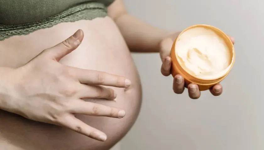 Ciało w ciąży, dłoń dotyka brzucha, druga trzyma krem. Delikatna pielęgnacja, może szczotkowanie na sucho w ciąży?