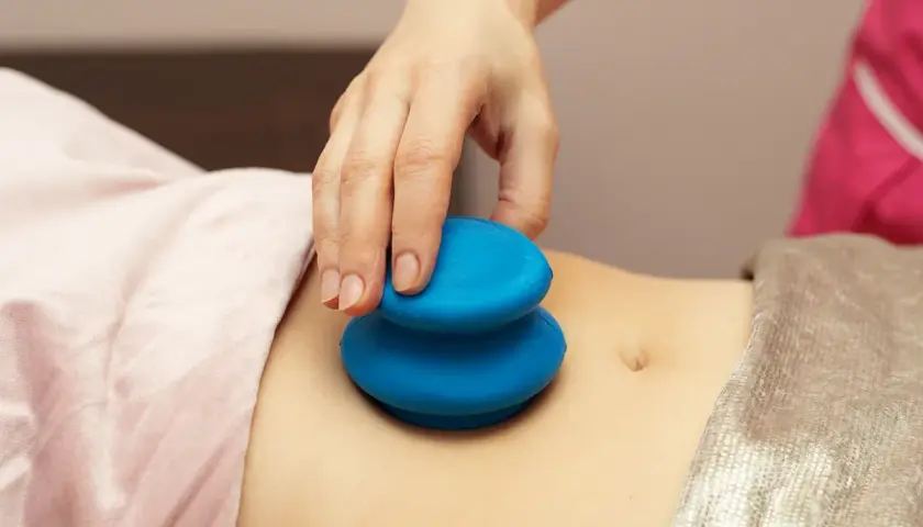 Dłoń terapeuty wykonuje masaż bańką chińską na brzuchu. Choć zabieg ma wiele zalet, warto znać jego potencjalne masaż bańką chińską efekty uboczne.