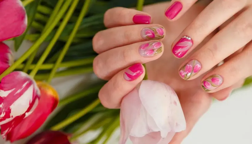 Dłonie z manicurem french zdobionym motywem tulipanów, otoczone bukietem różowych kwiatów.