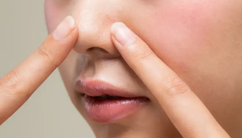 Dłonie dotykają nosa, ukazując drobne niedoskonałości i nadmiar sebum na twarzy.