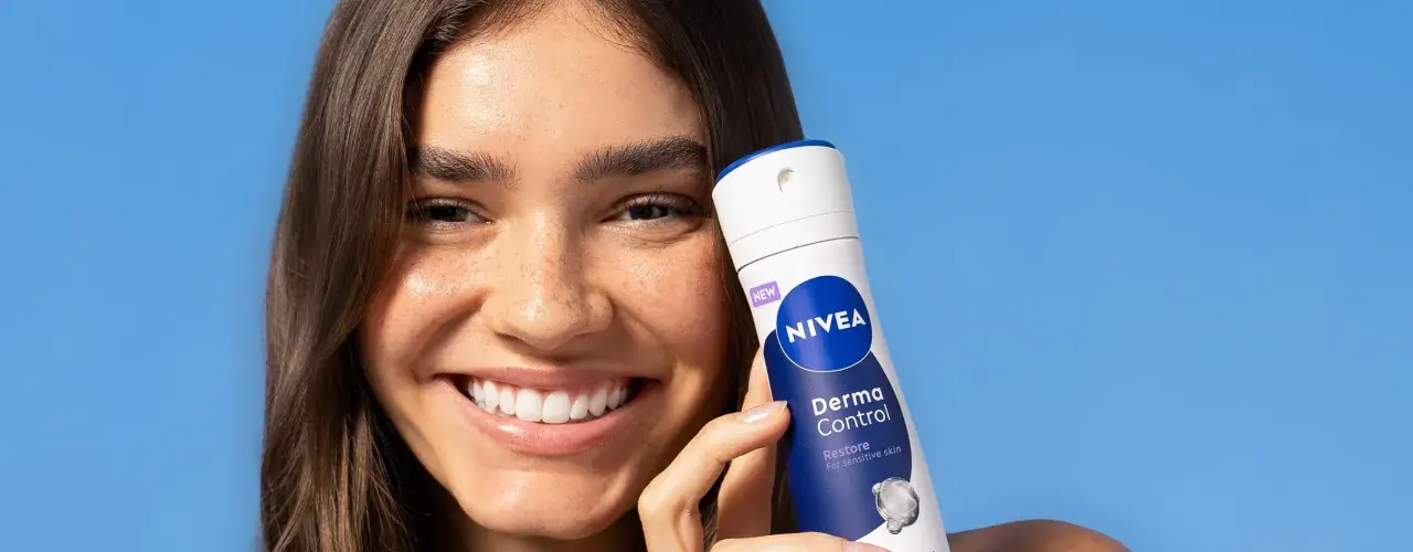 Uśmiechnięta kobieta trzyma NIVEA Derma Control, idealny produkt na swędzenie pod pachami.
