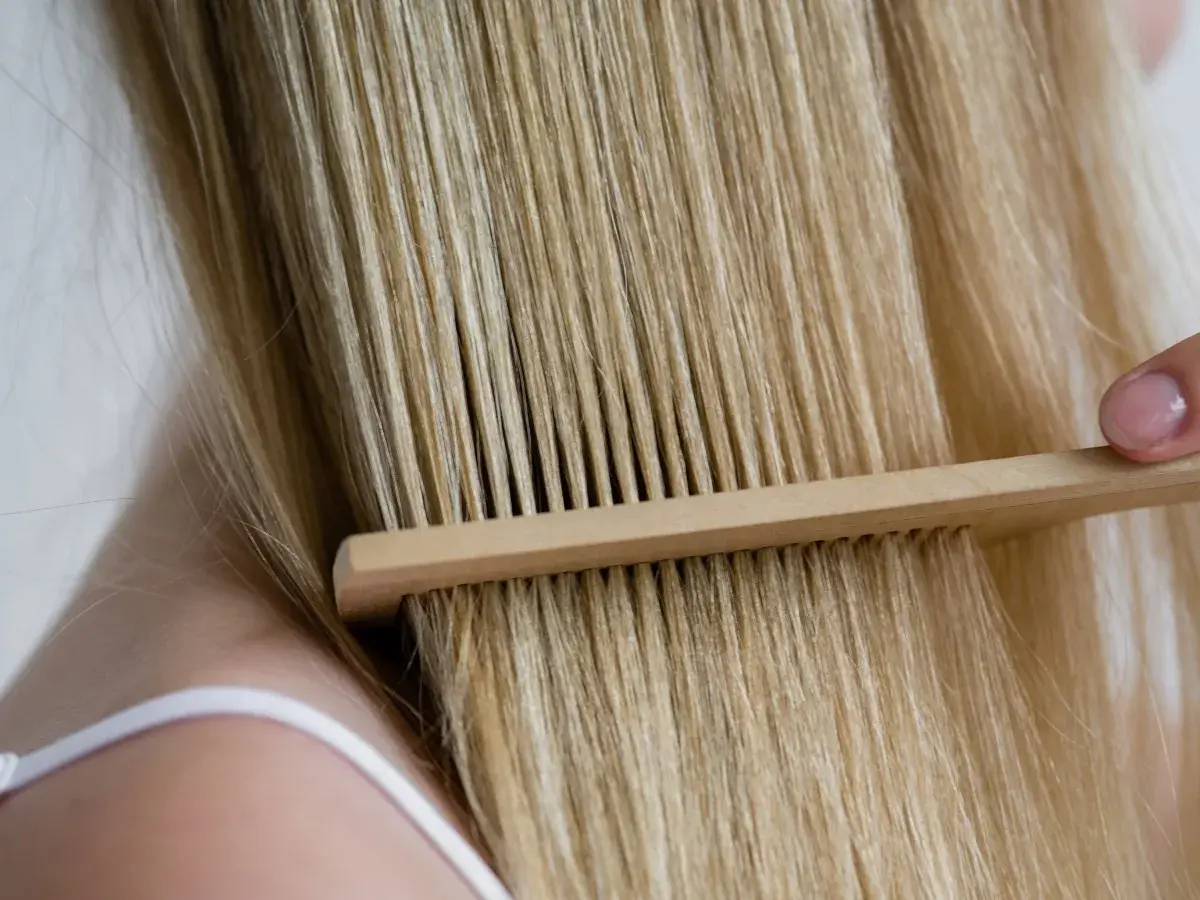 Delikatne rozczesywanie blond włosów drewnianym grzebieniem. Keratyna na co? Na zdrowe i lśniące włosy.