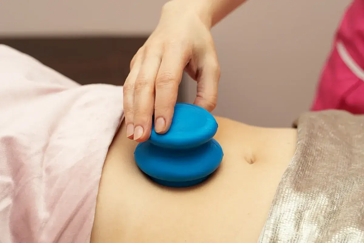 Dłoń terapeuty wykonuje masaż bańką chińską na brzuchu. Choć zabieg ma wiele zalet, warto znać jego potencjalne masaż bańką chińską efekty uboczne.