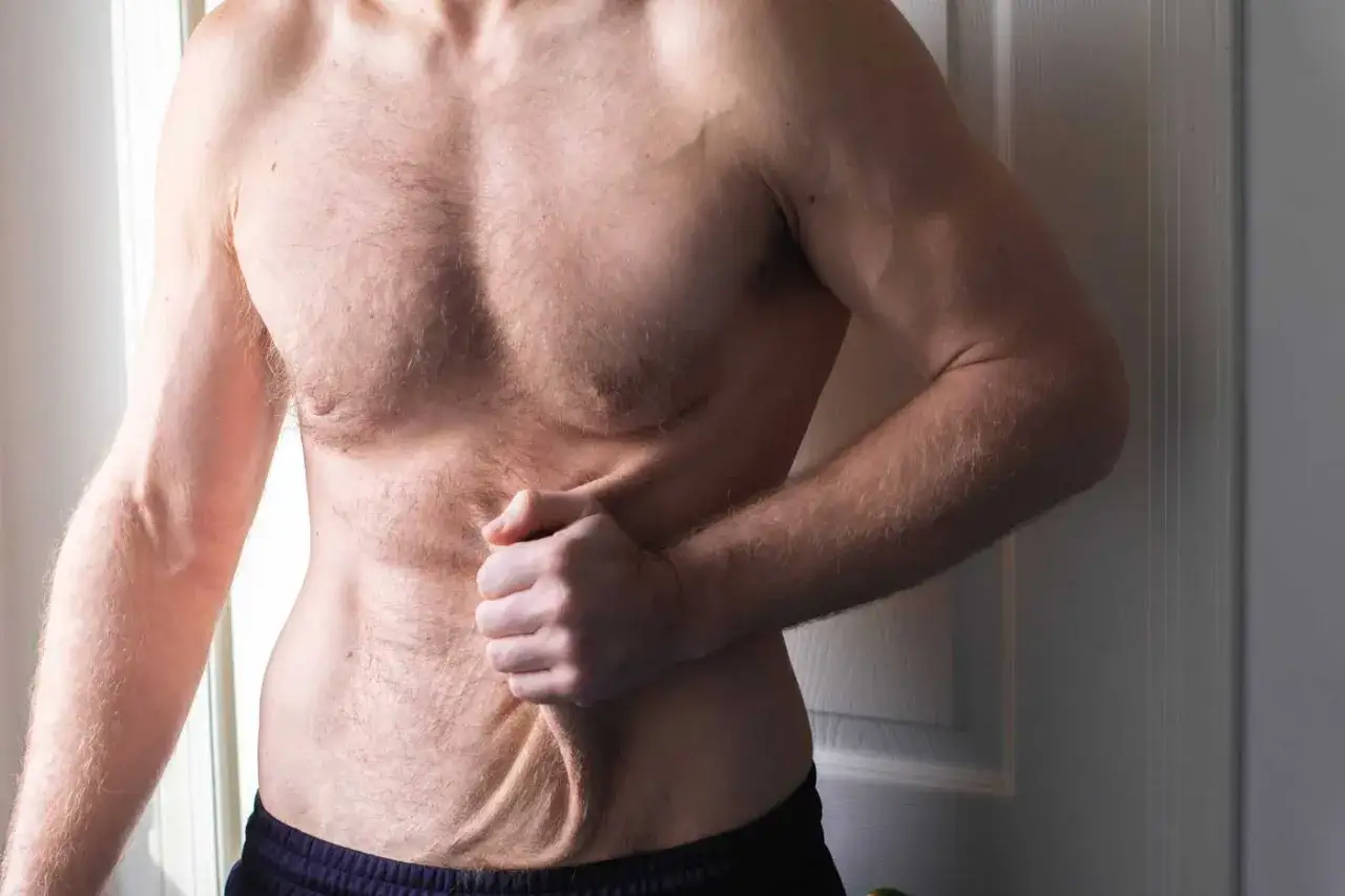 Mężczyzna pokazuje luźną sk&oacute;rę na brzuchu po schudnięciu 40 kg. Widoczne fałdy i nier&oacute;wności.